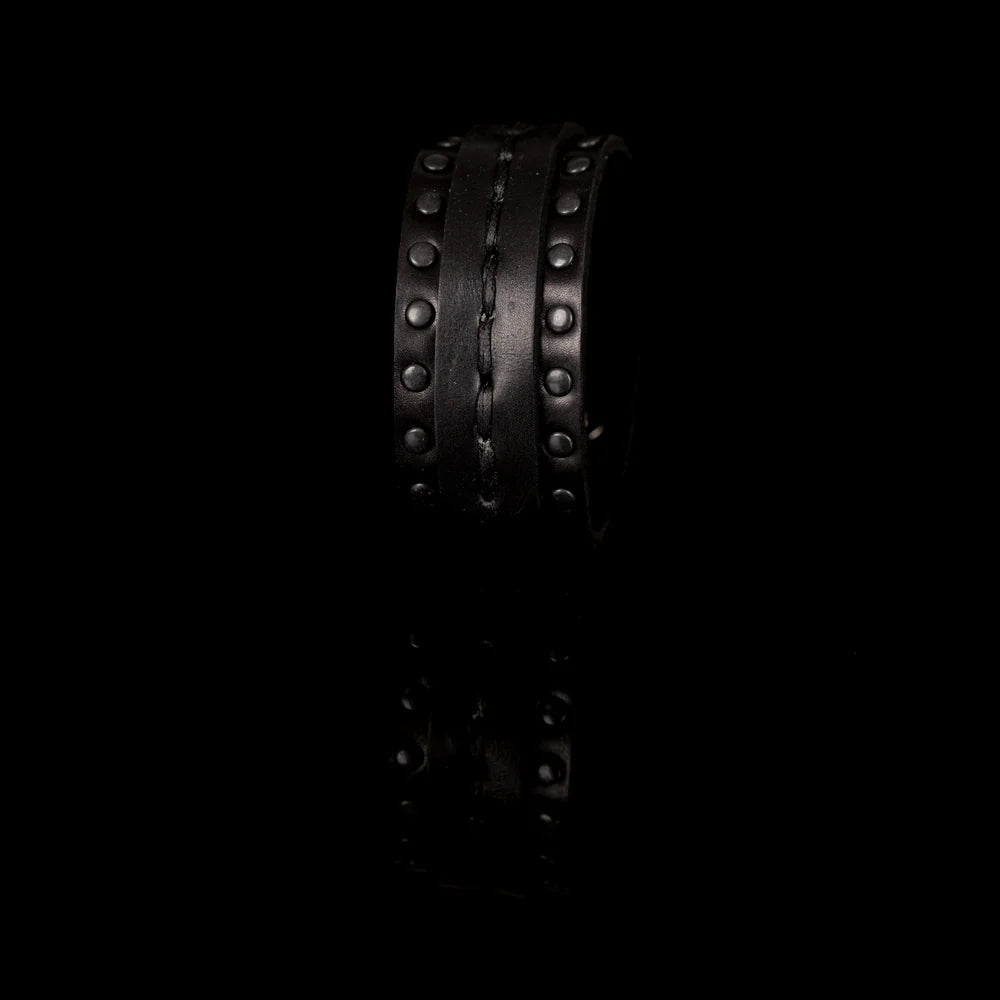 Black genuine leather cuff bracelet with hand-stitched center strap and black metal stud detailing, handcrafted statement accessory on a white background.
