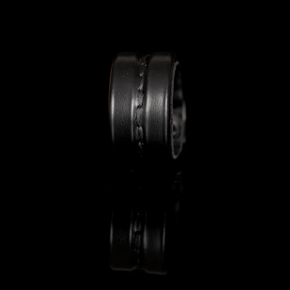 Black genuine leather cuff bracelet with a wide padded silhouette and handcrafted center stitching detail, minimalist statement accessory on a white background.