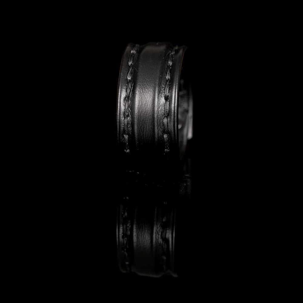 Black genuine leather cuff bracelet with a wide padded center panel and hand-stitched leather straps, photographed on a black reflective background with a luxury editorial look.