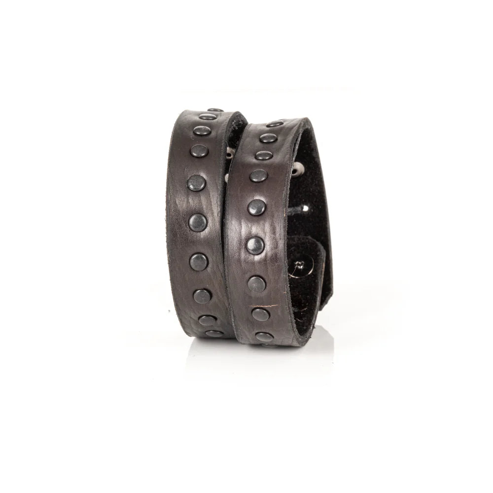 Black genuine leather wrap bracelet featuring double leather bands with black rivet detailing, handcrafted statement accessory with a rugged minimalist design, displayed on a white background.