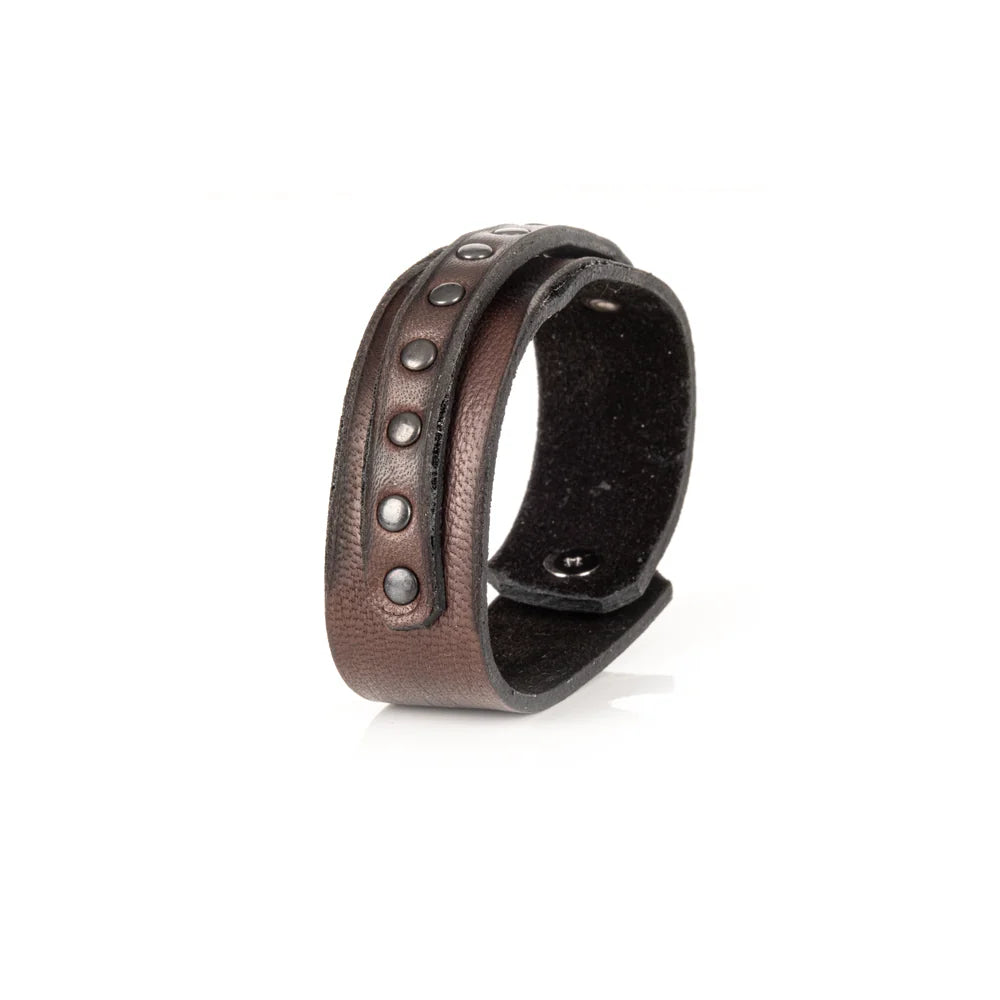 Men's handcrafted genuine leather cuff bracelet in dark brown featuring a wide minimalist design with a slim leather strip accented by matte black metal studs. Premium artisan men's leather wristband photographed on a clean white background.