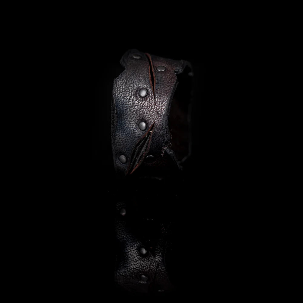 Black genuine leather cuff bracelet with sculpted cutout detailing, black rivet accents, and a handcrafted rugged artisan design, displayed on a white background.