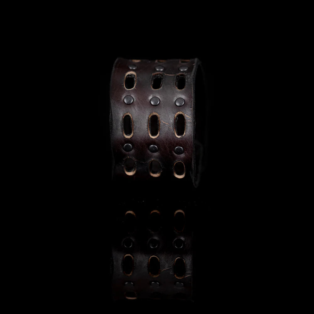 Black genuine leather cuff bracelet with perforated cutout detailing, black rivet accents, and a wide handcrafted statement design, displayed on a white background.
