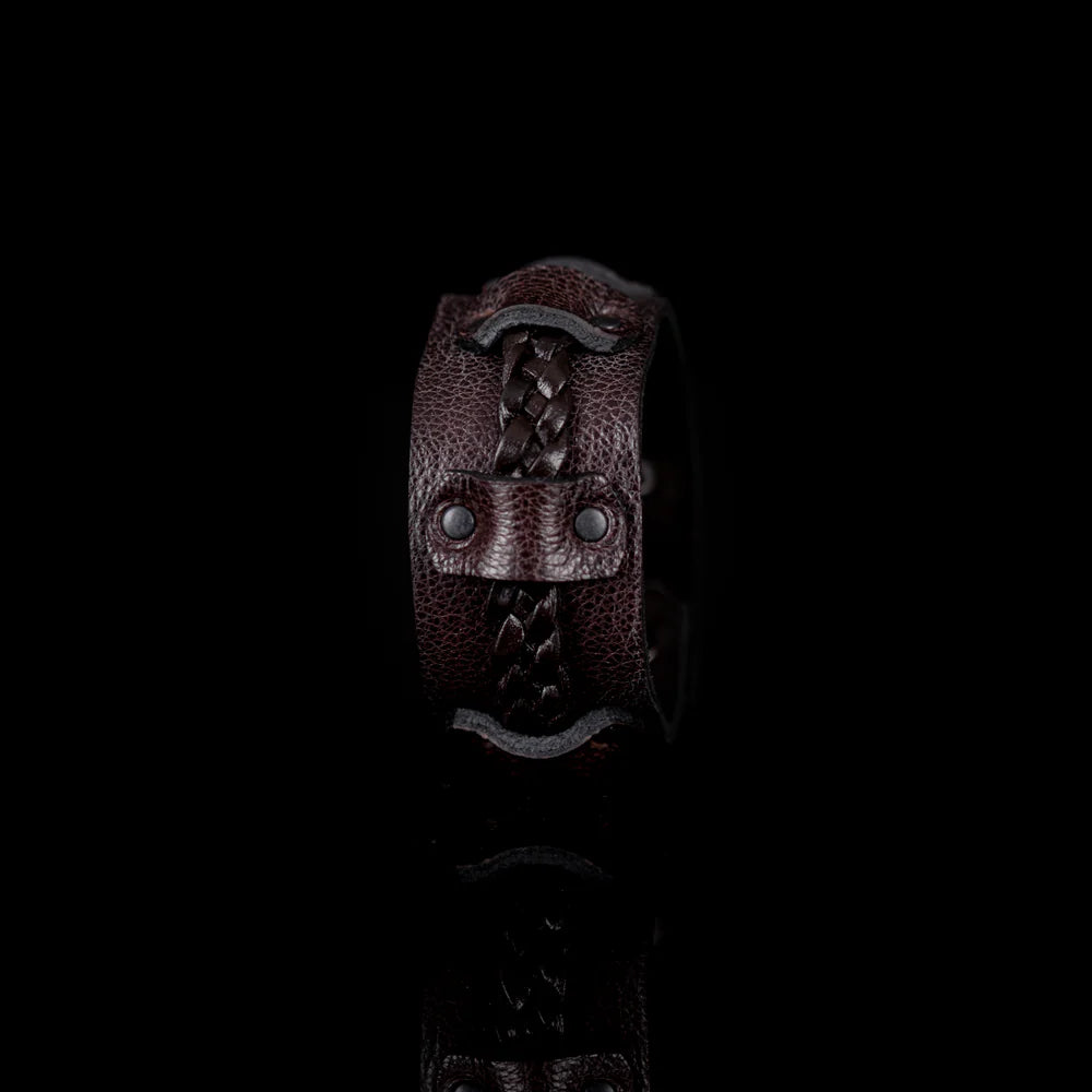 Men's handcrafted genuine leather cuff bracelet in dark brown featuring a wide leather band with a braided leather center strap, matte black rivet accents, and premium artisan craftsmanship. Luxury men's leather wristband photographed on a clean white background.