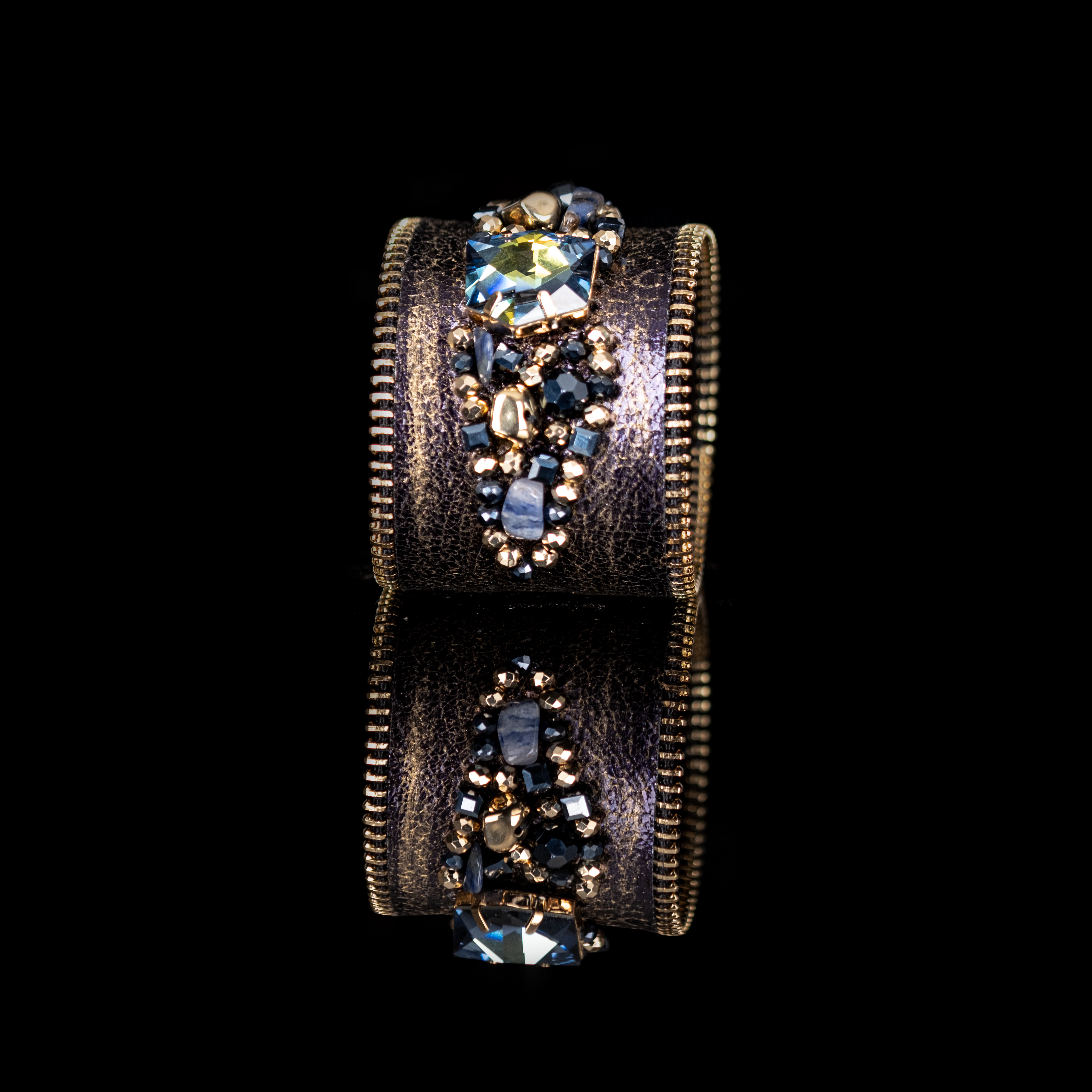 Dark leather cuff with gold brushed finish, zipper edges and blue-toned crystal cluster centerpiece