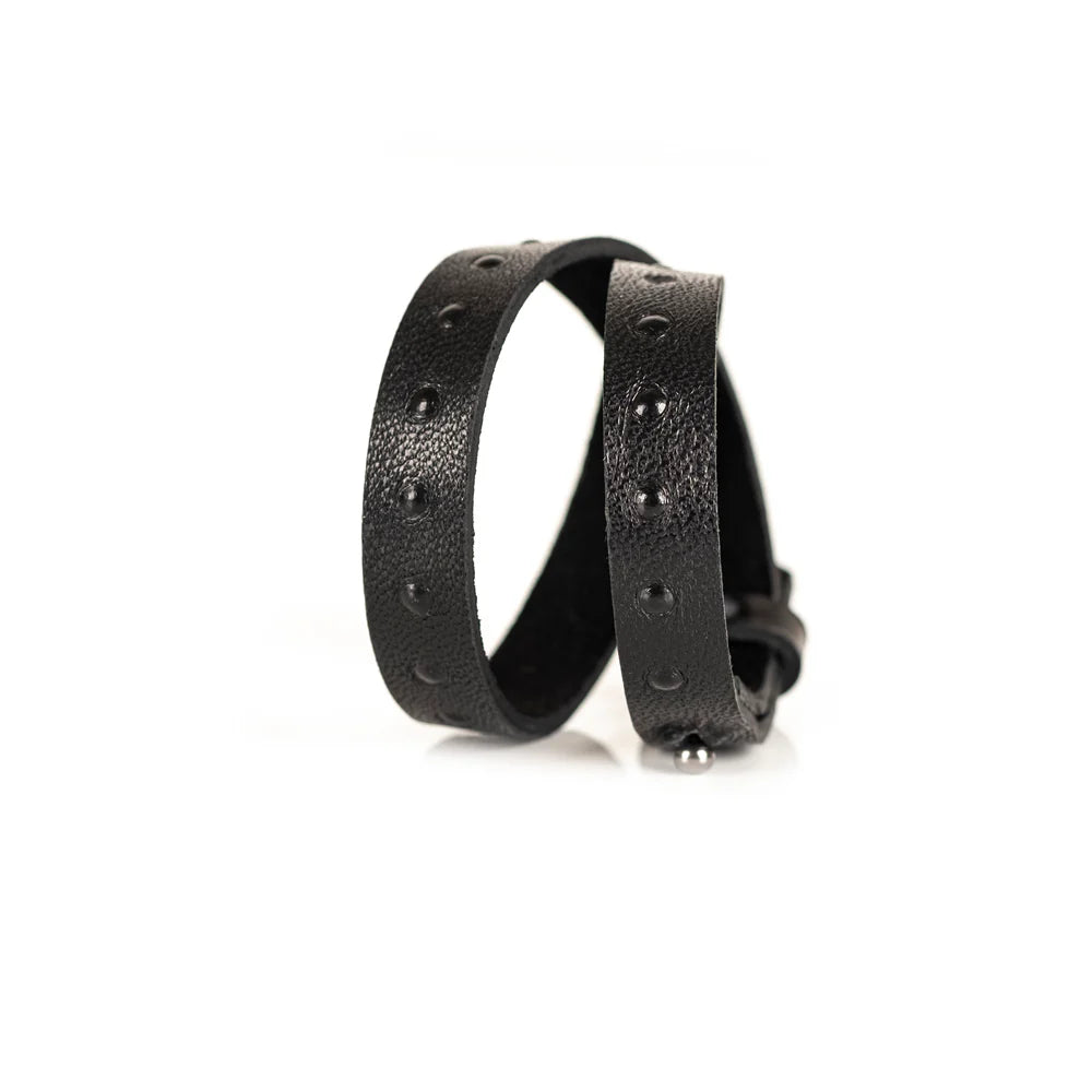 Black genuine leather wrap bracelet with embossed stud detailing and an adjustable strap closure, handcrafted minimalist accessory on a white background.