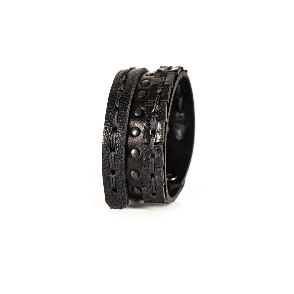 Black genuine leather bracelet featuring layered hand-stitched straps, black studded detailing, and geometric cut leather accents, handcrafted statement accessory on a white background.