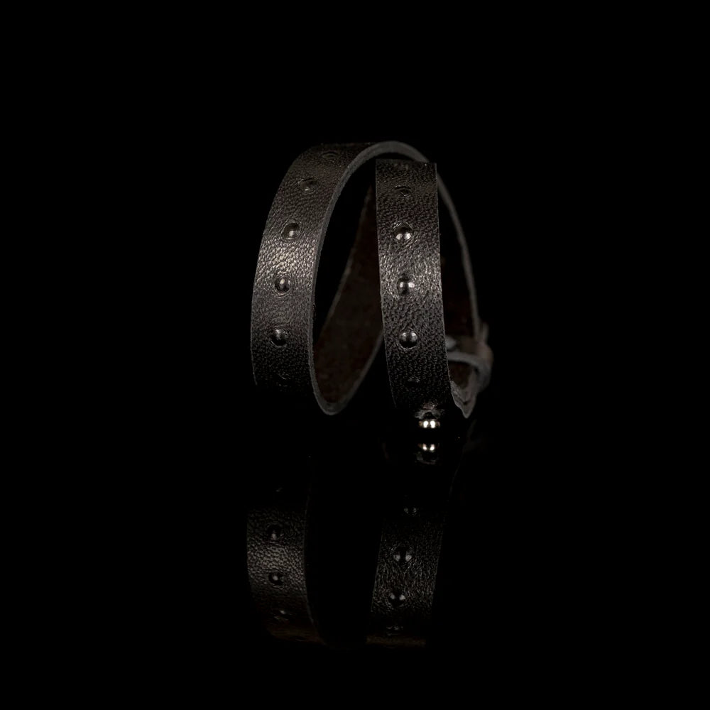 Black genuine leather wrap bracelet with embossed stud detailing and an adjustable strap closure, handcrafted minimalist accessory on a white background.