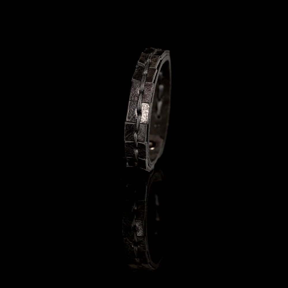 Black genuine leather bracelet featuring a hand-stitched center detail and geometric cut leather accents, handcrafted artisan accessory on a white background.