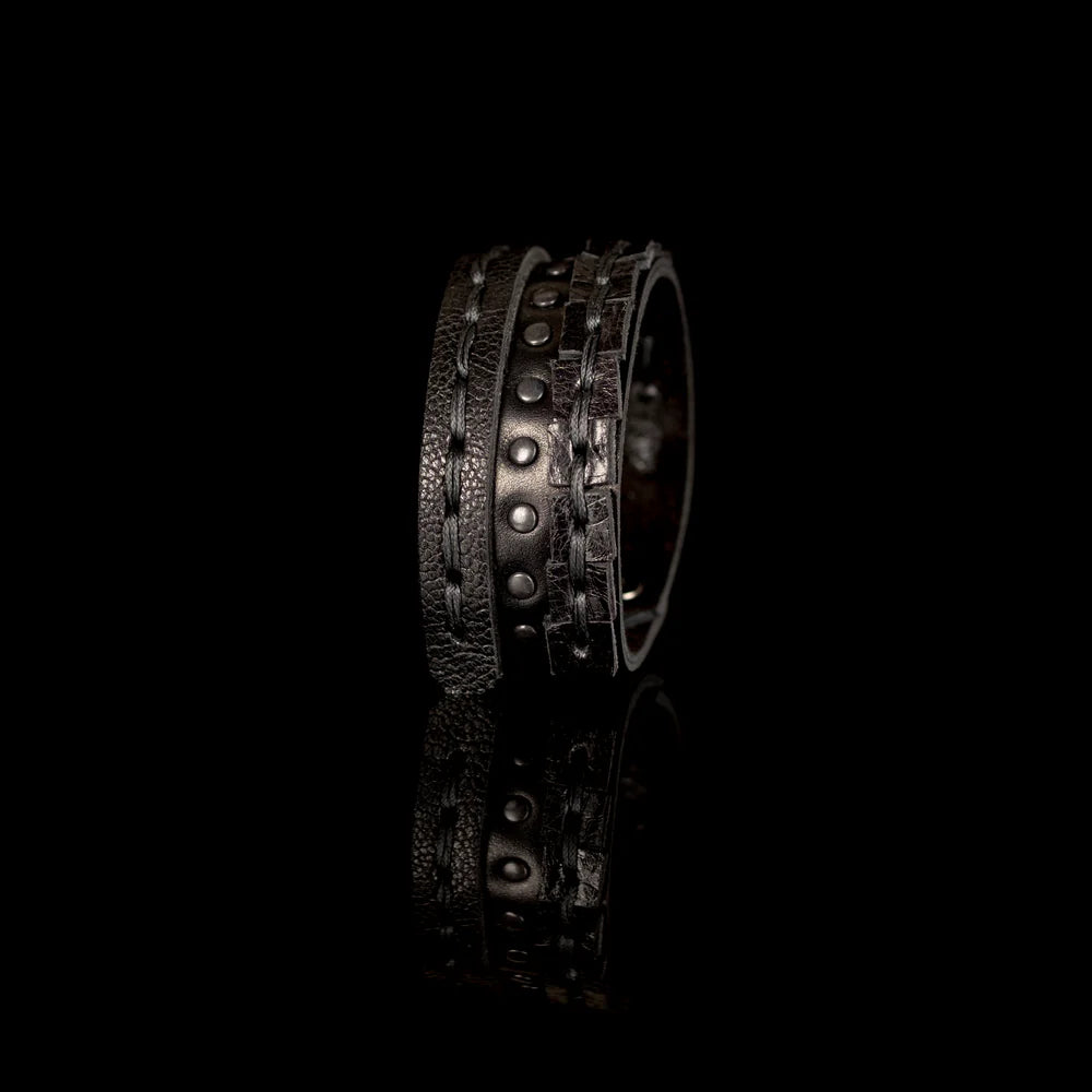 Black genuine leather bracelet featuring layered hand-stitched straps, black studded detailing, and geometric cut leather accents, handcrafted statement accessory on a white background.