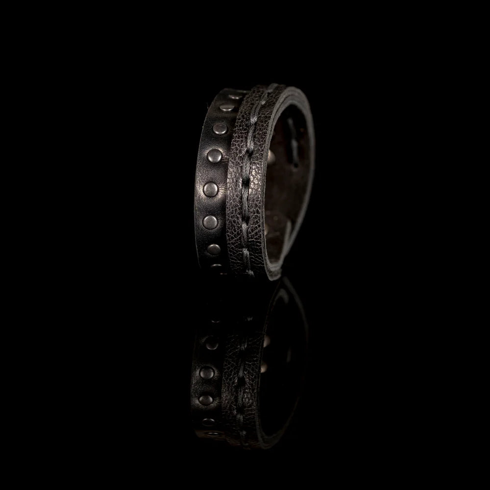 Black genuine leather bracelet featuring a hand-stitched leather band layered with a black studded strap, handcrafted statement accessory on a white background.