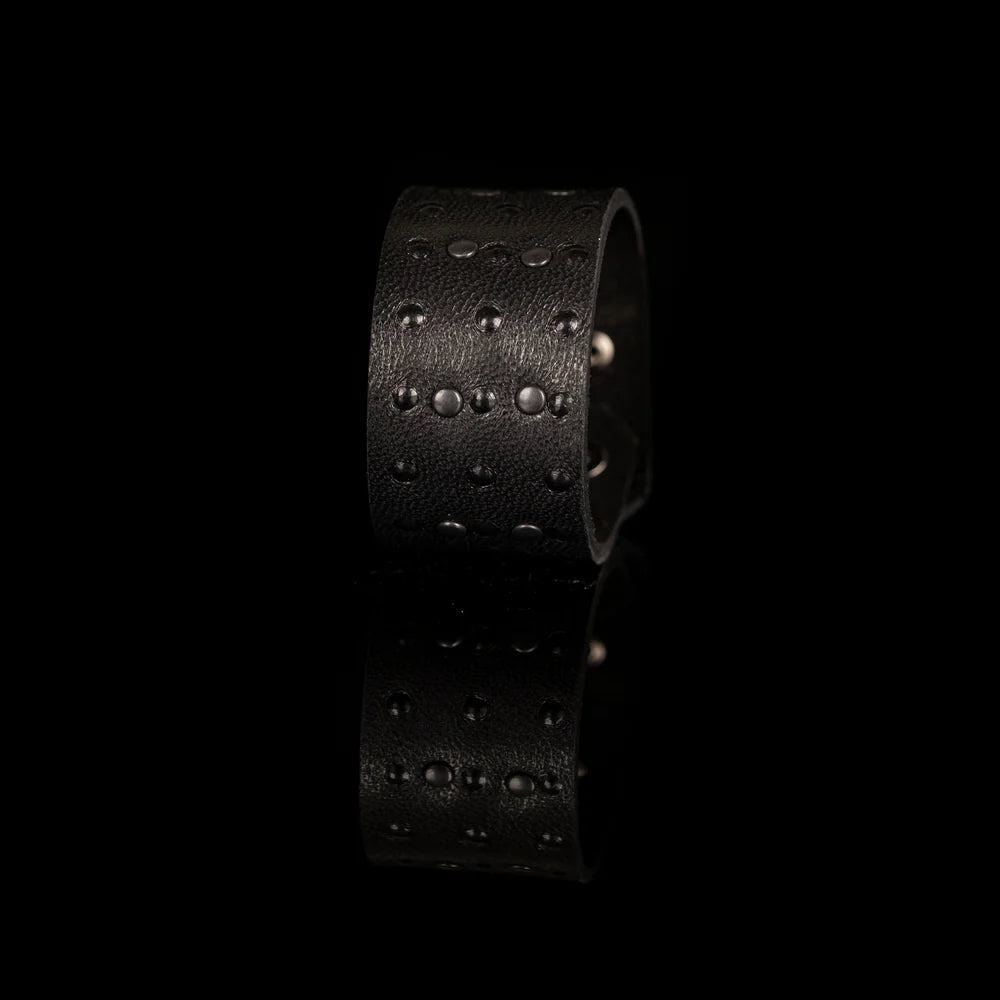 Black genuine leather cuff bracelet with black stud detailing arranged in a geometric pattern, handcrafted statement accessory with a textured leather finish on a white background.