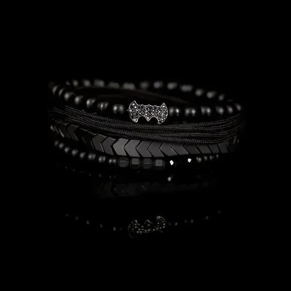 Men's layered black beaded bracelet set featuring matte black beads, hematite arrow-shaped beads, braided cord strands, faceted black crystal accents, and a black pavé bat-shaped centerpiece for a bold modern luxury style.