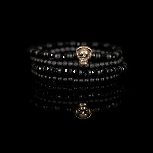 Black layered men’s bracelet set featuring matte black beads, faceted black crystal beads, and an antique gold skull centerpiece on a white background.