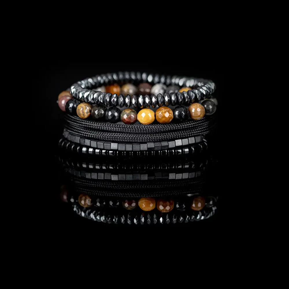 Layered men’s bracelet set featuring multicolor natural stone beads, faceted hematite beads, black hematite cube beads, braided black cord wraps, and glossy black disc beads, displayed on a white background.
