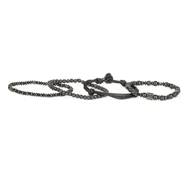 Men's layered black beaded bracelet set featuring matte black beads, lava stone beads, hematite spacers, braided cord strands, and a black pavé cubic zirconia accent bead for a modern luxury look.