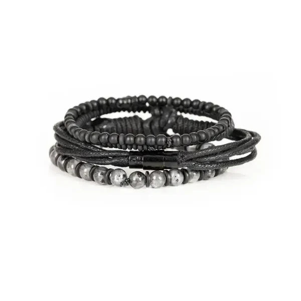 Men's layered black bracelet set featuring matte black beads, natural gray stone beads, braided leather cords, black wood beads, and hematite spacers in a rugged contemporary luxury design.