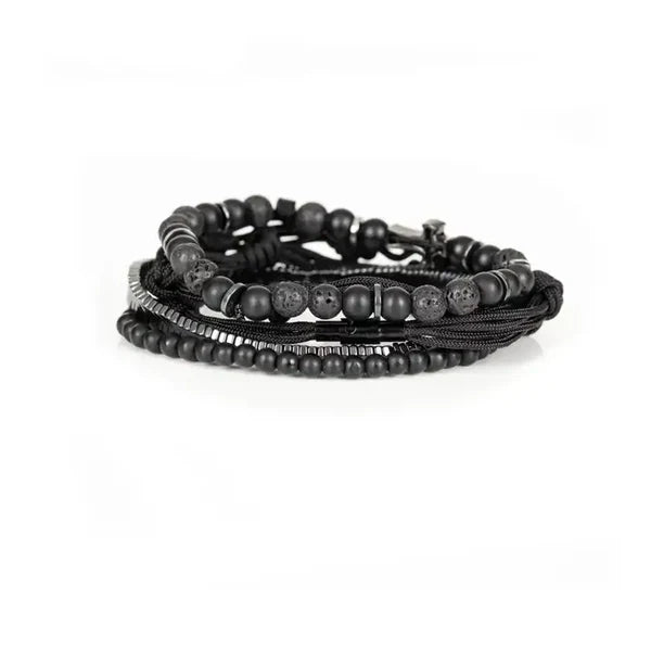 Black layered men’s bracelet with matte beads, braided cord knots, silver-tone chevron accents, and pavé cross centerpiece on a white background.